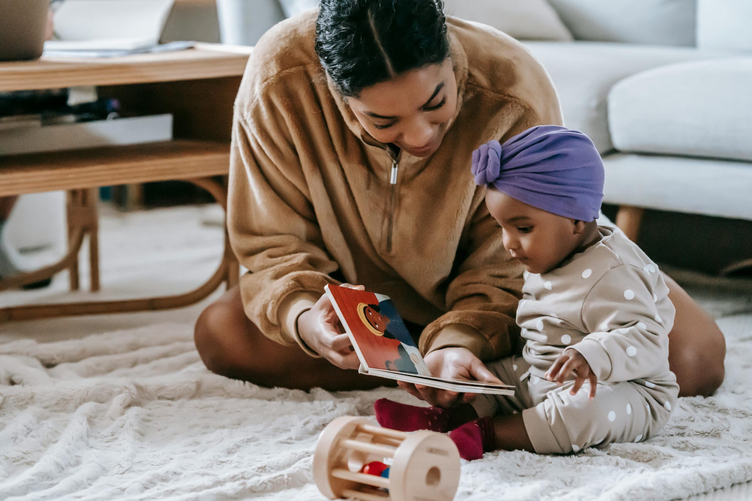 A mother and her baby bonding over a book on the floor of a cozy living room.